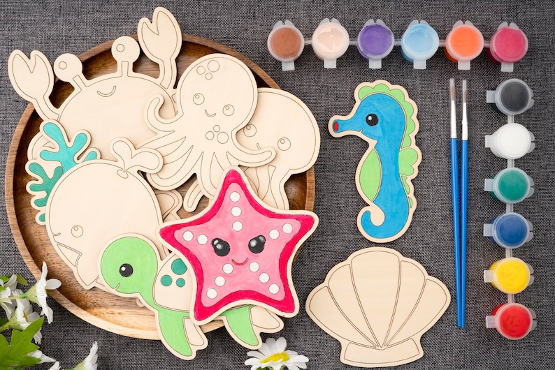 May include: A set of wooden sea creature shapes for painting. The set includes a crab, octopus, jellyfish, whale, turtle, starfish, and seashell. The shapes are unpainted and ready to be decorated with acrylic paints. The set also includes two paintbrushes and a variety of paint colors.