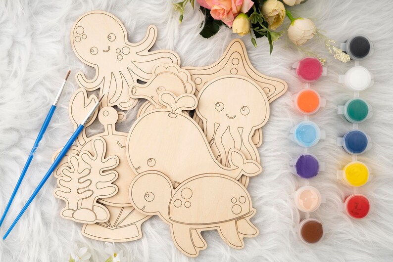May include: A set of wooden sea creature shapes for painting, including an octopus, a whale, a jellyfish, a seahorse, a turtle, and a starfish. The shapes are unpainted and ready to be decorated with paint. There are 10 small jars of paint in various colors.