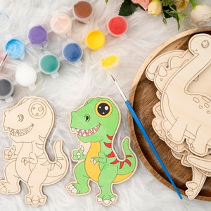 May include: Wooden dinosaur cutouts and paint set. The set includes several unpainted dinosaur shapes, paint pots in various colors, and paintbrushes. One dinosaur is painted green, yellow, and red. The set is designed for arts and crafts.