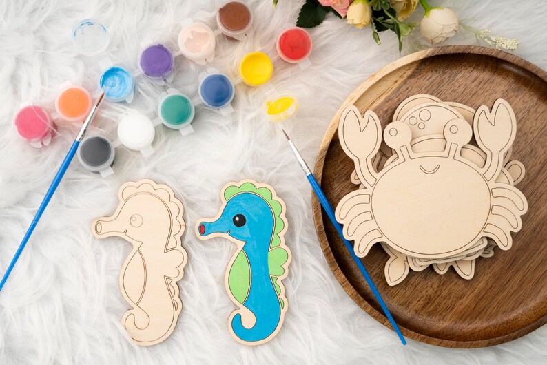 May include: A set of wooden craft kits featuring a seahorse, a crab, and paint pots. The seahorse is light blue with green accents, and the crab is natural wood. The paint pots are various colors, including red, blue, green, yellow, and white.