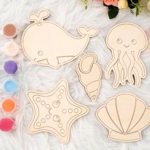 May include: A set of five wooden sea creature shapes for painting, including a whale, a jellyfish, a seashell, a starfish, and a seashell. The shapes are unpainted and ready to be decorated with paint.