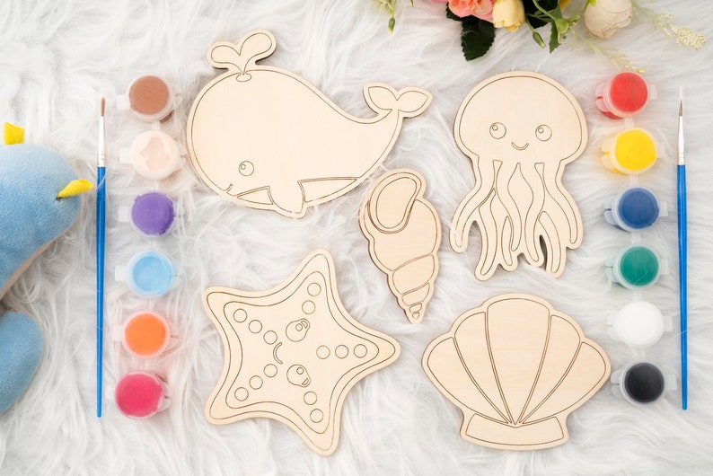 May include: A set of five wooden sea creature shapes for painting, including a whale, a jellyfish, a seashell, a starfish, and a seashell. The shapes are unpainted and ready to be decorated with paint.