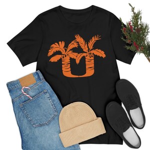 May include: Black t-shirt with an orange graphic of two palm trees forming the letter "U".