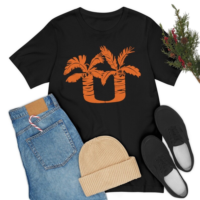 May include: Black t-shirt with an orange graphic of two palm trees forming the letter "U".