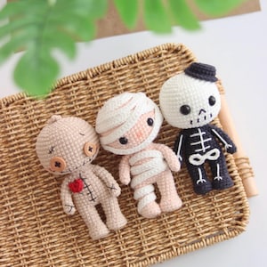 Op de afbeelding: Drie handgemaakte gehaakte poppen: een voodoopop, een mummie en een skelet. De voodoopop is bruin met knoopogen en een rood hart. De mummie is gewikkeld in wit en roze garen. Het skelet is wit en zwart en draagt een kleine hoed.