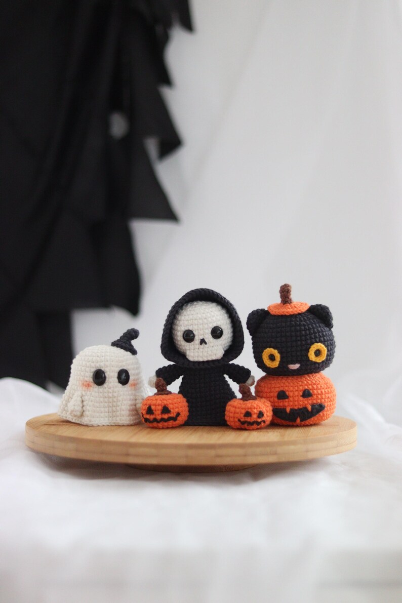 May include: Crocheted Halloween decorations on a wooden tray. Includes a white ghost, a black-robed skeleton holding two orange pumpkins, and a black cat atop an orange pumpkin. The decorations are handmade and suitable for Halloween.