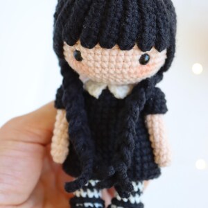 May include: Crocheted doll with black hair, a black dress, and white collar. The doll has black eyes, rosy cheeks, and black and white striped stockings. The doll is a handmade craft item.