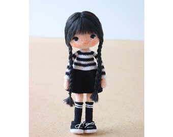 May include: A crocheted doll with black hair, a black and white striped shirt, a black skirt, black and white striped socks, and black shoes.