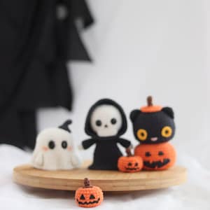 May include: A collection of handmade crochet Halloween decorations. Includes a white ghost, a black Grim Reaper, a black cat with an orange pumpkin body, and two orange pumpkins. The figures are displayed on a wooden tray.