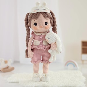 Peut inclure: Poupée au crochet faite à la main, vêtue d'une tenue rose et d'un masque de sommeil à oreilles de lapin. Elle tient un petit lapin blanc. La poupée a des tresses brunes et se tient sur un tapis blanc.