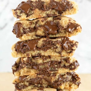 May include: A stack of five chocolate chip cookies, cut in half to reveal a rich, gooey chocolate center. The cookies are golden brown with visible chocolate chips and a generous amount of melted chocolate. The image is a close-up shot.