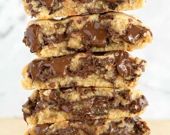 May include: A stack of five chocolate chip cookies, cut in half to reveal a rich, gooey chocolate center. The cookies are golden brown with visible chocolate chips and a generous amount of melted chocolate. The image is a close-up shot.