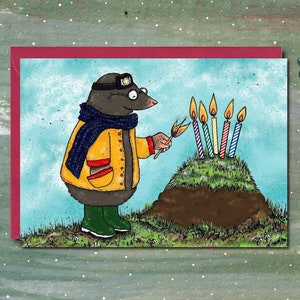 May include: A cartoon mole wearing a yellow jacket and blue scarf lights the candles on a birthday cake. The cake is a mound of dirt with five lit candles.