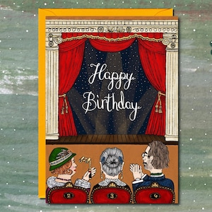 May include: A greeting card with a red and gold colour scheme. The card features a stage with red curtains and a spotlight shining on the text "Happy Birthday". Three people are sitting in the audience, watching the show.