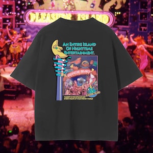 May include: Black t-shirt with a colorful graphic featuring a crescent moon, stars, and the words "AN ENTIRE ISLAND OF NIGHTTIME ENTERTAINMENT." The graphic also includes the text "PLEASURE ISLAND" and "VARIETY IS THE SPICE OF LIFE EVERY NIGHT AT WALT DISNEY WORLD."