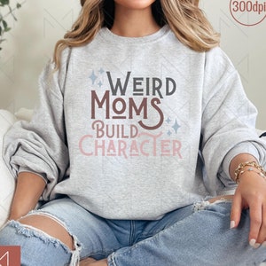 May include: A grey sweatshirt with the text "Weird Moms Build Character" in pink and brown lettering with glitter accents.