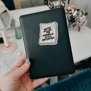 May include: A black e-reader with a sticker on it that says "WANTED WITCH KILLER THE HUMAN IS STILL INSIDE HIM".