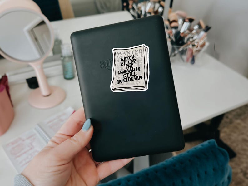 May include: A black e-reader with a sticker on it that says "WANTED WITCH KILLER THE HUMAN IS STILL INSIDE HIM".