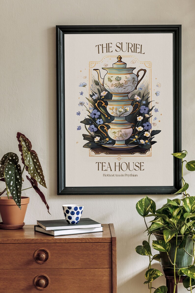 May include: A black framed poster with a vintage illustration of a tea set with a teapot and three cups stacked on top of each other. The poster has the text "The Suriel Tea House" and "Hottest tea in Prythian".