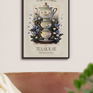 May include: A vintage-style poster with a black frame featuring a stack of teacups and a teapot with floral designs. The poster reads "The Suriel Tea House" and "Hottest tea in Prythian".