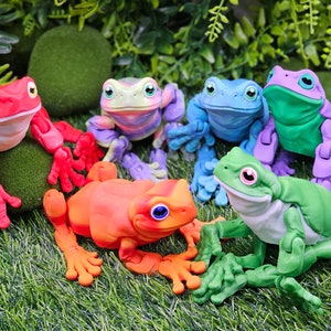 May include: Six colourful frog figurines with articulated limbs. The frogs are posed in a sitting position and are made of a smooth, painted material. The frogs are red, orange, yellow, green, blue, and purple.