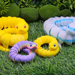May include: Four colourful segmented snake toys made of soft, flexible material. The snakes are yellow, blue and white, and purple and green. The toys are arranged on a bed of green grass.