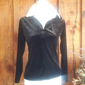 Puede incluir: Camiseta de manga larga de terciopelo negro con cuello blanco y cierre de cremallera.