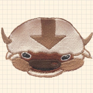 May include: Embroidered patch of Appa, the sky bison from Avatar: The Last Airbender. The patch is brown and white with a brown arrow on the forehead.