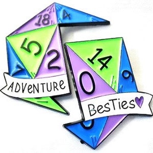 May include: Two colorful enamel pins shaped like dice with numbers on each side. The first die has the numbers 5, 2, 18, and 4. The second die has the numbers 14, 0, and 9. The first die has a banner that says "Adventure" and the second die has a banner that says "Bestiez" with a heart.