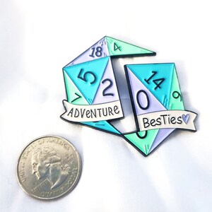May include: Two enamel pins shaped like dice with the numbers 18, 5, 2, 14, 0, and 9. The dice are green, purple, and blue. The pins have the words "Adventure" and "BestTies" written on them.