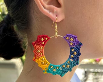 May include: Rainbow colored crocheted hoop earrings with gold beads and a gold hook. The earrings are hanging from a person's ear.