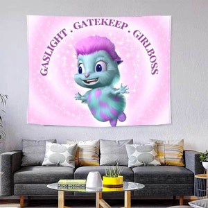 Peut inclure: Une tapisserie rose avec une créature de dessin animé bleue et violette avec une crête rose. La tapisserie porte le texte "Gaslight. Gatekeep. Girlboss" en cercle autour de la créature.