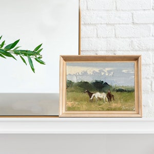 Puede incluir: Una pintura enmarcada de un paisaje con dos caballos en un campo. Los caballos son marr&oacute;n y blanco, y el campo es verde con un cielo azul en el fondo.