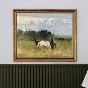 Puede incluir: Una pintura al &oacute;leo enmarcada que representa tres caballos en un campo. Los caballos son marr&oacute;n, blanco y marr&oacute;n. El fondo es un campo verde con un cielo azul y nubes blancas.