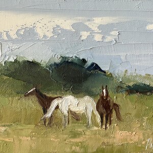 Puede incluir: Una pintura de tres caballos en un campo con una cordillera de monta&ntilde;as en el fondo. Los caballos son marrones y blancos, y el cielo es de un azul claro con nubes blancas.