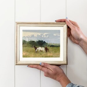 Puede incluir: Una pintura enmarcada de un paisaje con dos caballos en un campo. La pintura est&aacute; realizada en un estilo suelto e impresionista, con un enfoque en los caballos y el cielo. Los colores son apagados y terrosos, con tonos de verde, marr&oacute;n y azul.
