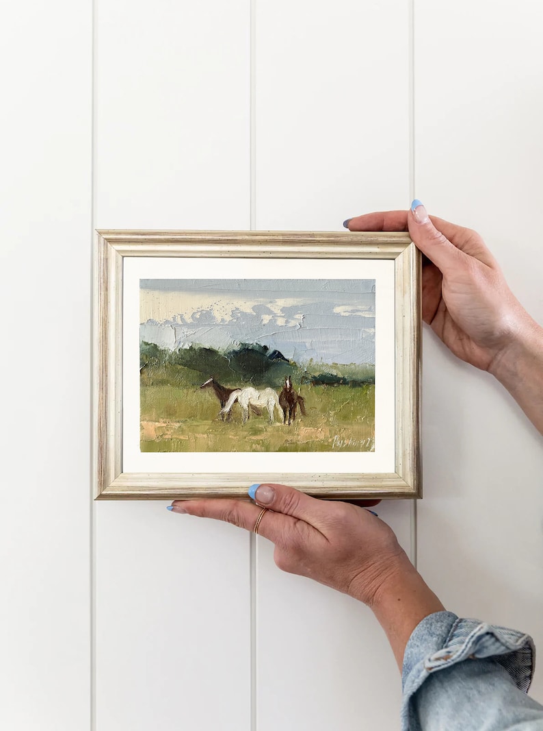 Puede incluir: Una pintura enmarcada de un paisaje con dos caballos en un campo. La pintura est&aacute; realizada en un estilo suelto e impresionista, con un enfoque en los caballos y el cielo. Los colores son apagados y terrosos, con tonos de verde, marr&oacute;n y azul.