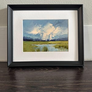 K&ouml;nnte beinhalten: Gerahmtes Landschafts-&Ouml;lgem&auml;lde mit einem lebendigen Himmel mit wei&szlig;en Wolken und einem gr&uuml;nen Feld. Das Kunstwerk ist in einem schwarzen Rahmen mit wei&szlig;em Passepartout gefasst, was einen auff&auml;lligen Kontrast erzeugt. Das Gem&auml;lde zeigt eine ruhige Szene im Freien.