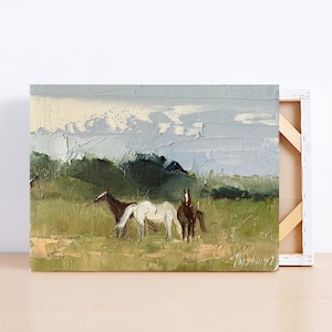 Puede incluir: Una pintura de tres caballos en un campo con una cordillera de monta&ntilde;as en el fondo. Los caballos son marr&oacute;n, blanco y marr&oacute;n. El cielo es de un azul claro con nubes blancas.