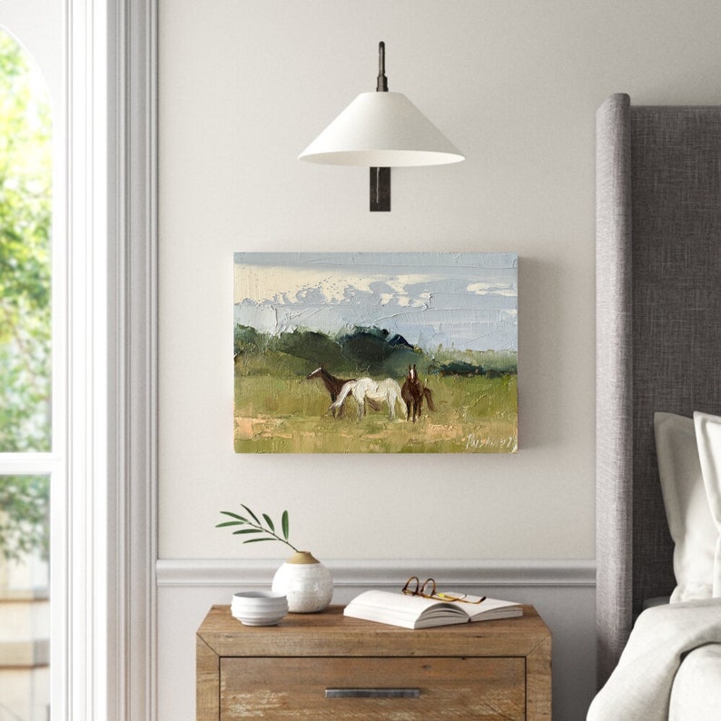 Puede incluir: Una pintura de tres caballos en un campo con un cielo azul y colinas verdes en el fondo.