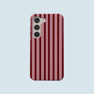 May include: A mobile phone case featuring a vertical striped design in burgundy and pale pink. The case has a camera module with three lenses. The phone case is rectangular with rounded corners.