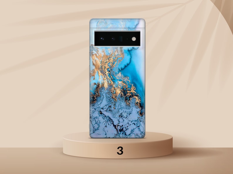 May include: A blue and gold marble phone case with a camera cutout. The case is on a light brown pedestal with the number 3 printed on it.