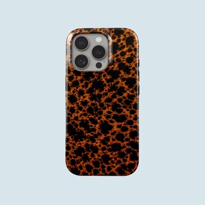 Może przedstawiać: Etui na telefon z wzorem skorupy żółwia. Etui ma błyszczące wykończenie i powtarzający się wzór czarnych plam na ciepłym, pomarańczowo-brązowym tle. Obiektywy aparatu są widoczne na górze.