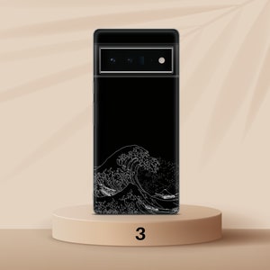 Puede incluir: Funda negra para tel&eacute;fono con un gr&aacute;fico blanco de una ola. La funda est&aacute; sobre un pedestal marr&oacute;n claro con el n&uacute;mero 3 impreso.