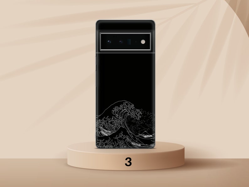 Puede incluir: Funda negra para tel&eacute;fono con un gr&aacute;fico blanco de una ola. La funda est&aacute; sobre un pedestal marr&oacute;n claro con el n&uacute;mero 3 impreso.