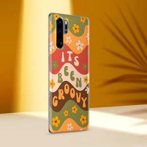 May include: A phone case with a groovy 70s style design. It features a wavy pattern in shades of orange, red, green, and brown with yellow flowers. The text "It's Been Groovy" is printed in a retro font.