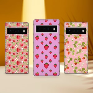 Può includere: Tre custodie per telefono rosa con diversi motivi di fragole. La prima custodia ha uno sfondo rosa con fragole bianche e api. La seconda custodia ha uno sfondo rosa con fragole bianche. La terza custodia ha uno sfondo rosa con fragole bianche e fiori bianchi.