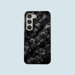 Peut inclure: Coque de téléphone noire avec un motif de dentelle florale détaillé. L'étui a une finition brillante et un module caméra avec trois objectifs. Le design est une esthétique sombre et élégante, adaptée à divers styles.