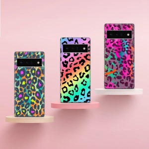 May include: Three phone cases with different leopard print designs. The cases are all black with colorful leopard spots. The phone cases are on a pink background.