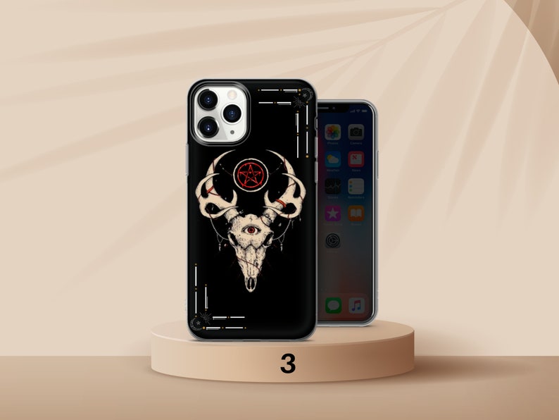 K&ouml;nnte beinhalten: Schwarze Handyh&uuml;lle mit einem wei&szlig;en Sch&auml;deldesign, einem roten Pentagramm und einem Auge. Die H&uuml;lle befindet sich auf einem kleinen, runden, hellbraunen Sockel. Ein zweites Telefon ist rechts zu sehen.